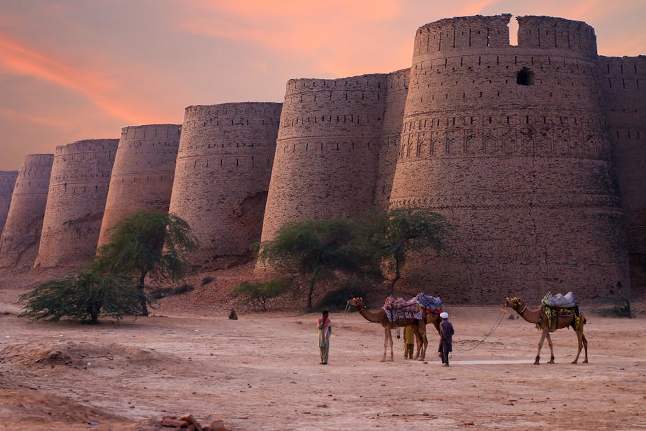 Scenic view of Derawar Fort's towers at sunset in the Punjab desert with camels and people.